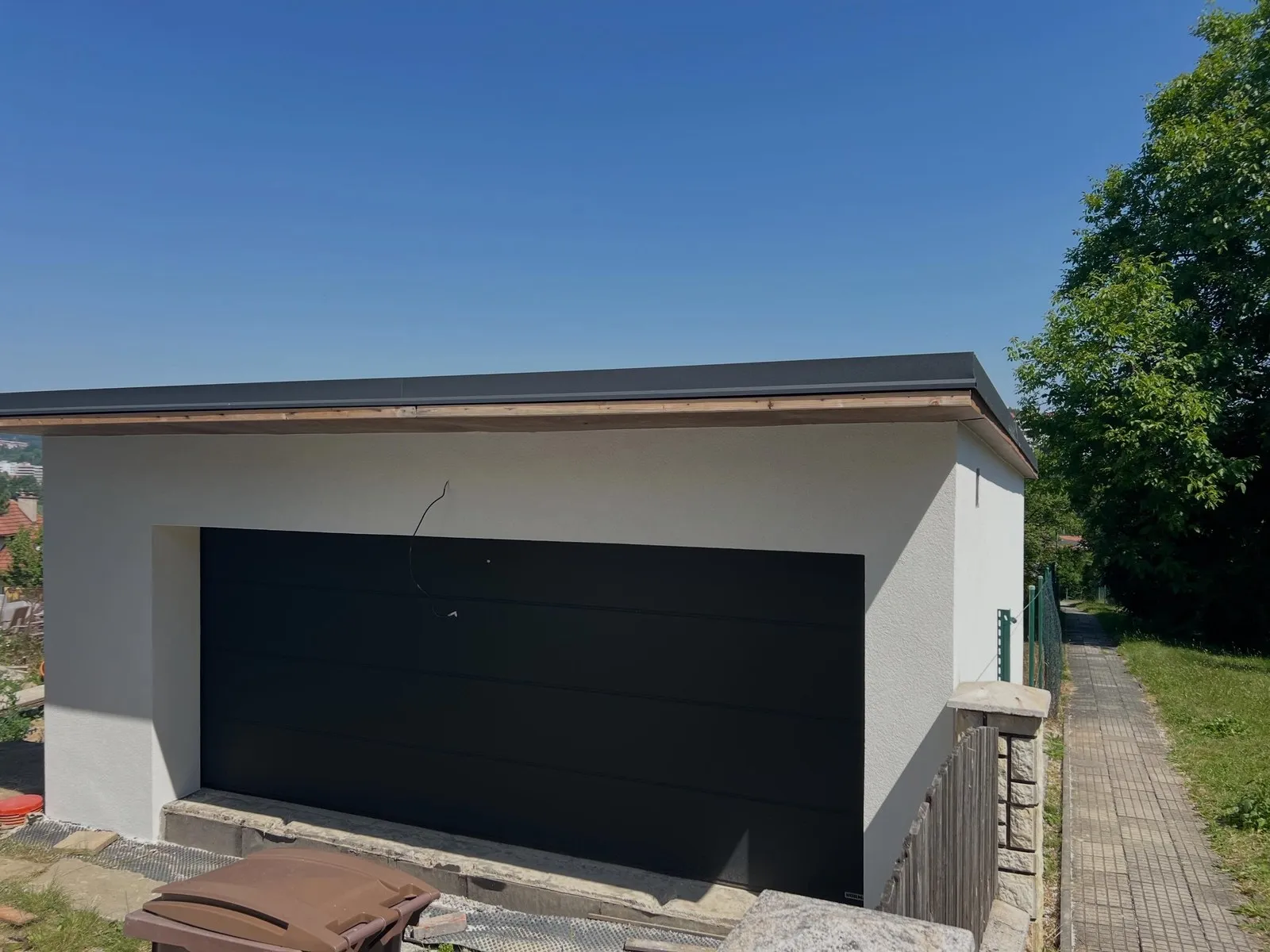 Dokončená garáž s bílou fasádou a tmavými sekčními vraty